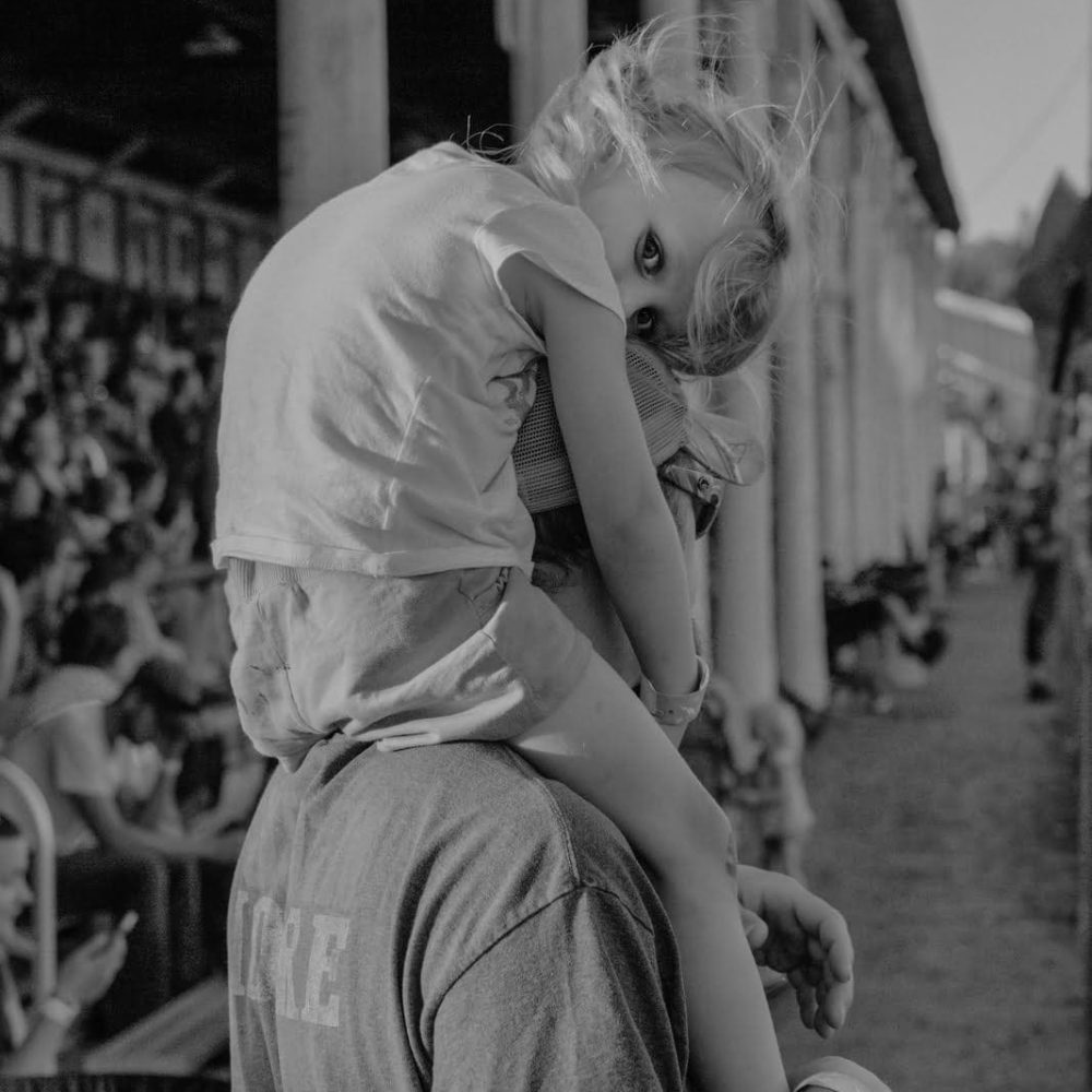 Fotografia Documentaria 2023 | FrancescoMerlini 06 | Spazi Fotografici Sandusky, Michigan, USA. Sanilac County fair. A young spectator on the shoulder of her father during a rear wheel drive figure 8 race.